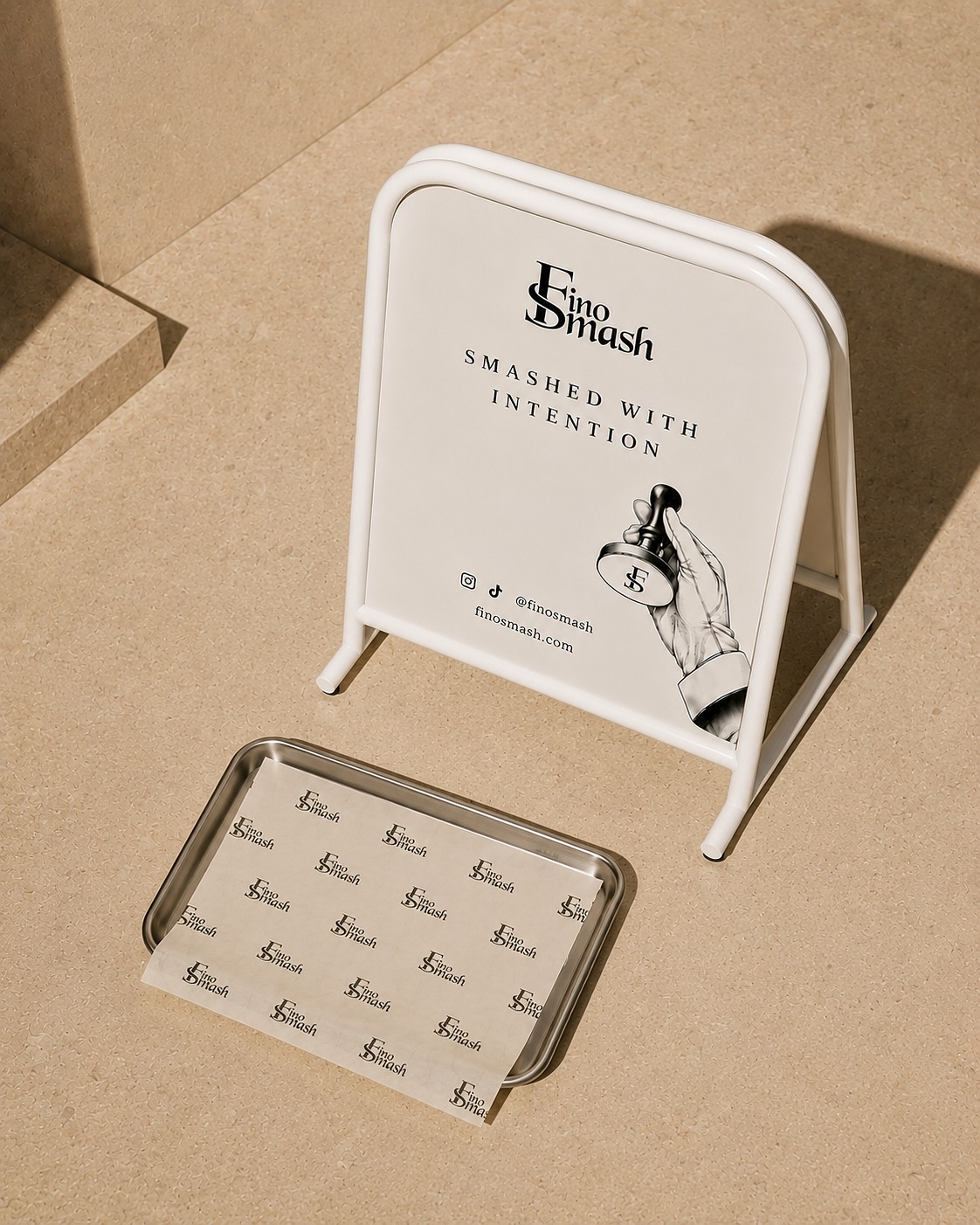 FinoSmash campaign: a cream A-board reading Smashed with intention beside a steel tray lined with FinoSmash paper, shot from above